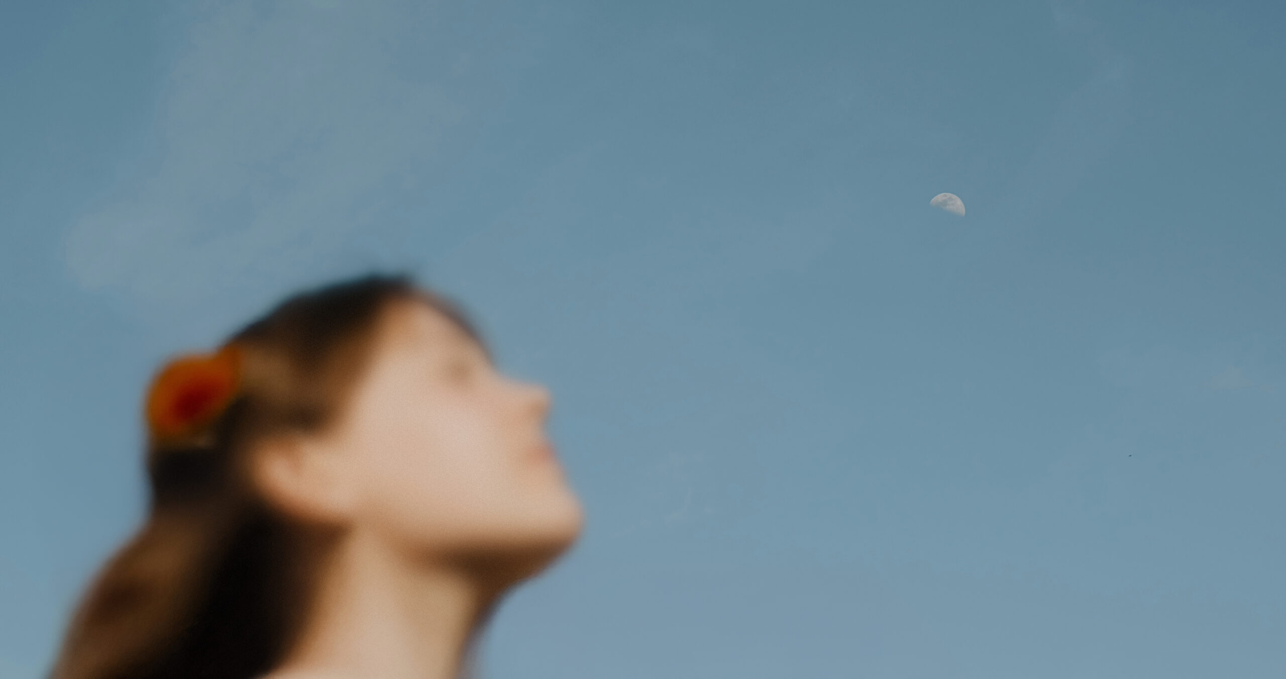 Blue sky with a half moon at top right corner and a person's out of focus profile in the bottom right corner